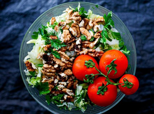 Top view of a fresh mixed salad with walnuts and tomatoes in a glass bowl, emphasizing healthy eating.