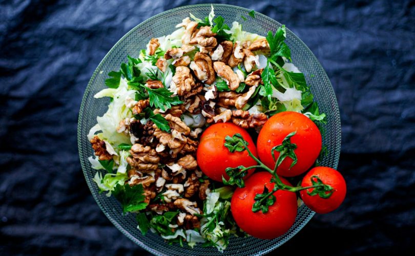 Top view of a fresh mixed salad with walnuts and tomatoes in a glass bowl, emphasizing healthy eating.