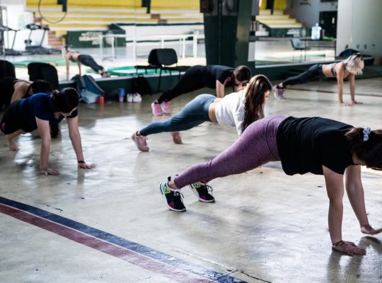 Group of women doing push-ups in a gym reflecting in a mirror.
