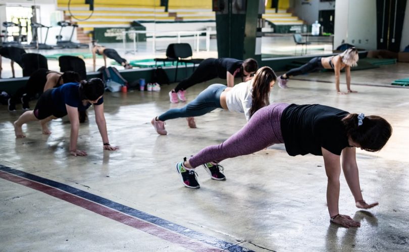 Group of women doing push-ups in a gym reflecting in a mirror.